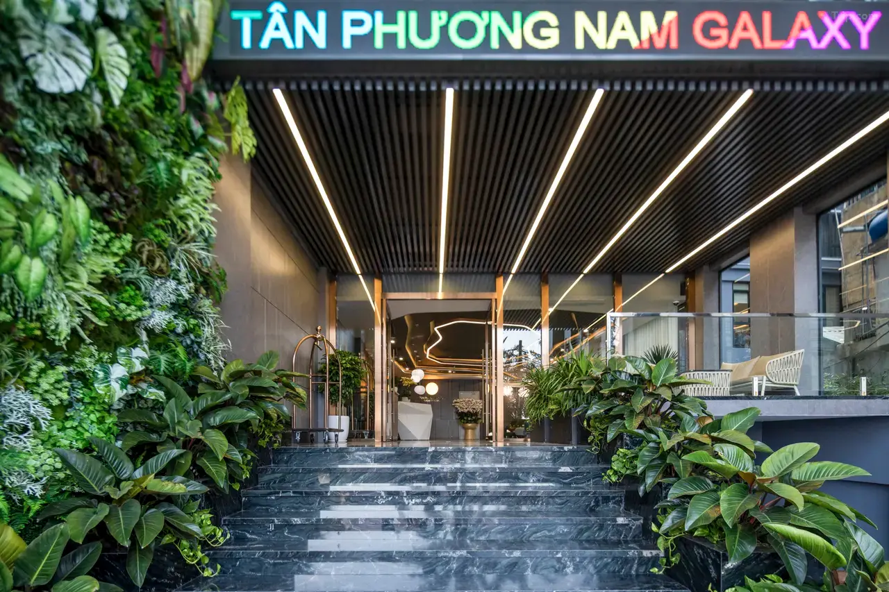 대리석 계단 위로 ‘TÂN PHƯƠNG NAM GALAXY’ 네온 간판과 식물 벽이 이어지는 호텔 출입구